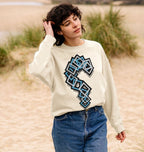 Woman wearing a cream graphic sweatshirt with blue geometric design and blue jeans, Comfy Elegance