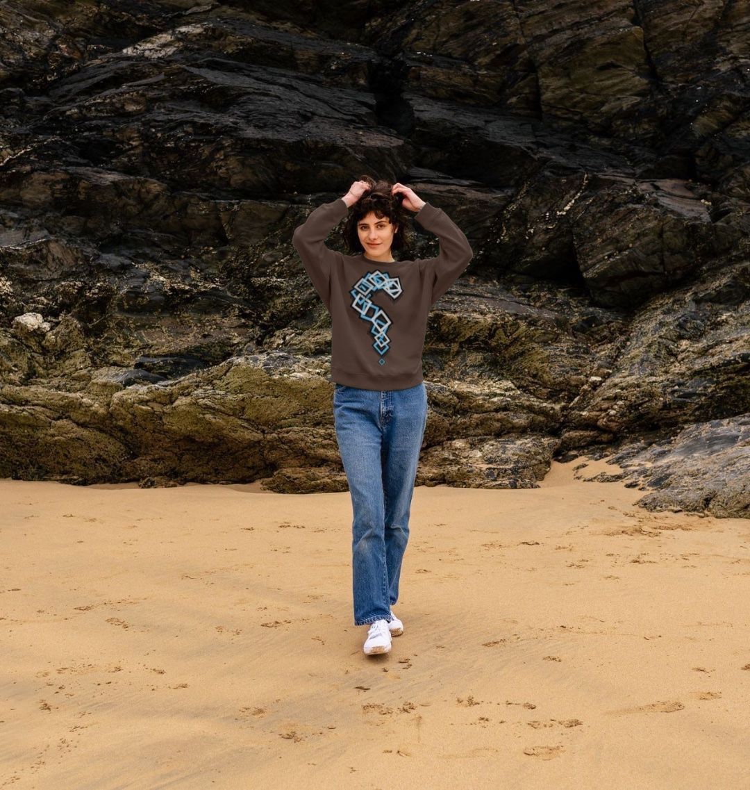 Woman wearing a brown graphic sweatshirt and blue jeans on a beach, Comfy Elegance